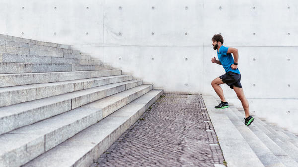 A man in a blue shirt, running shorts and bright shoes is running up wide concrete steps outdoors.  
